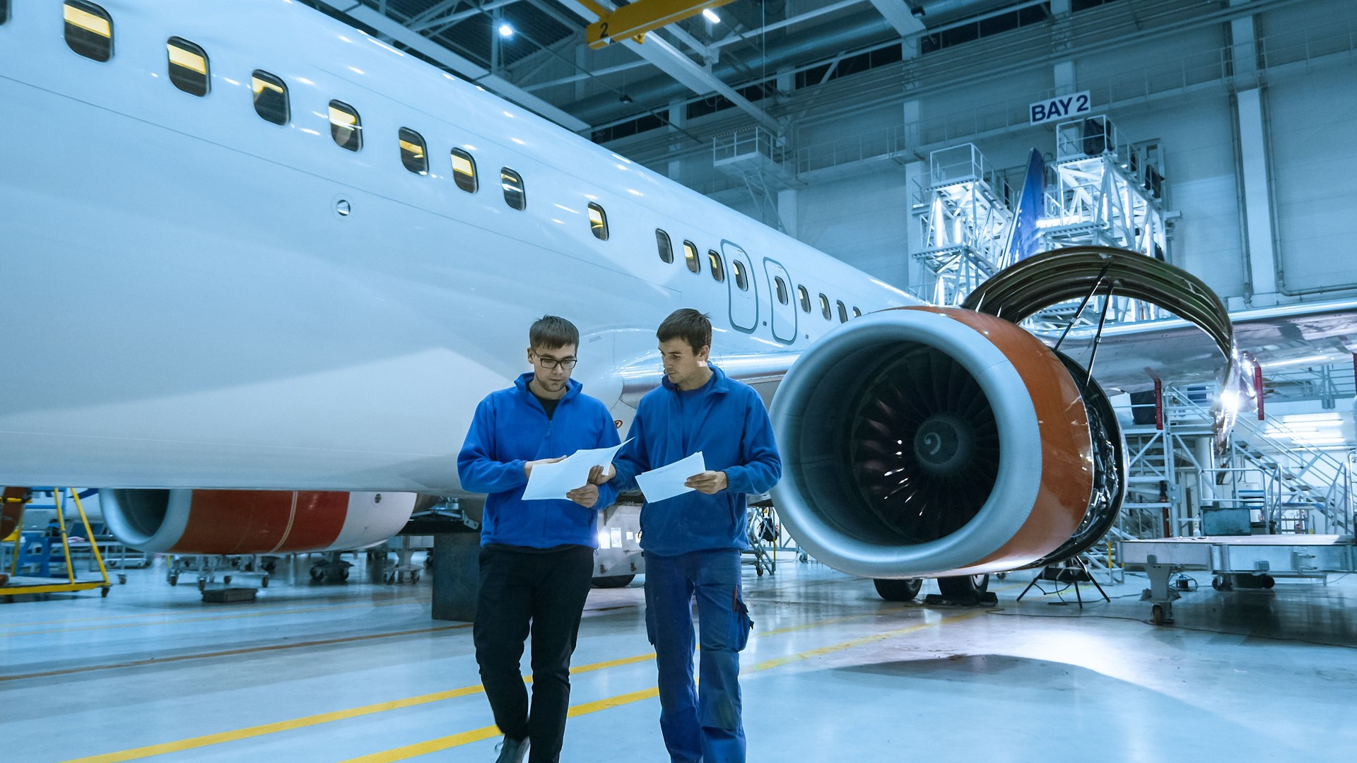 Aircraft maintenance mechanic uses tablet in front of a airplane cabin in a hangar.